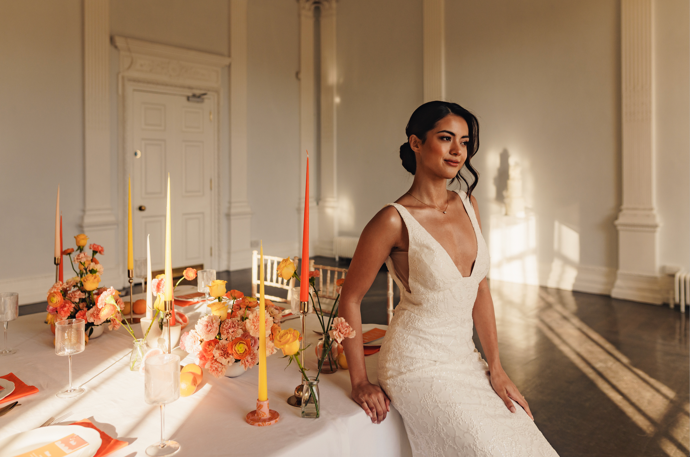 A bride leaning on a wedding-decorated table and slightly looking away.